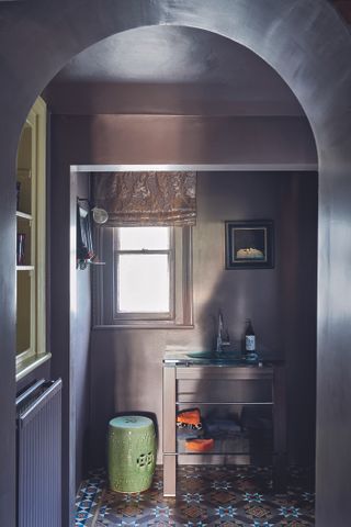 A bathroom painted purple with a small wash basin and a vintage framed art work on the wall