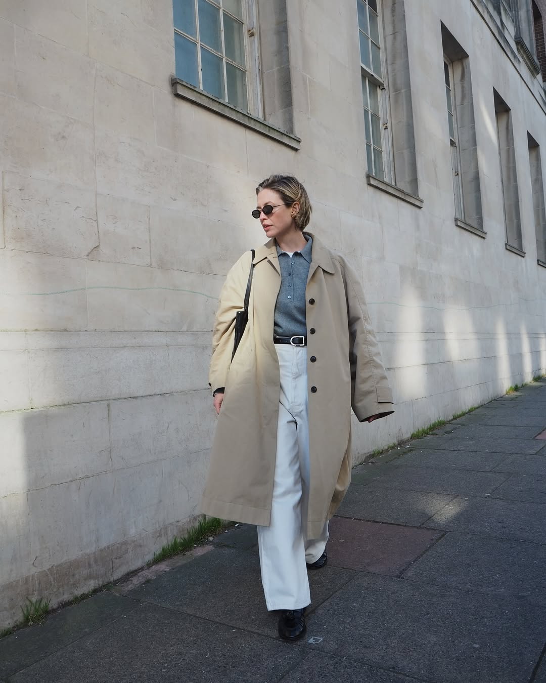 Alexis in white jeans, black loafers and a trench coat