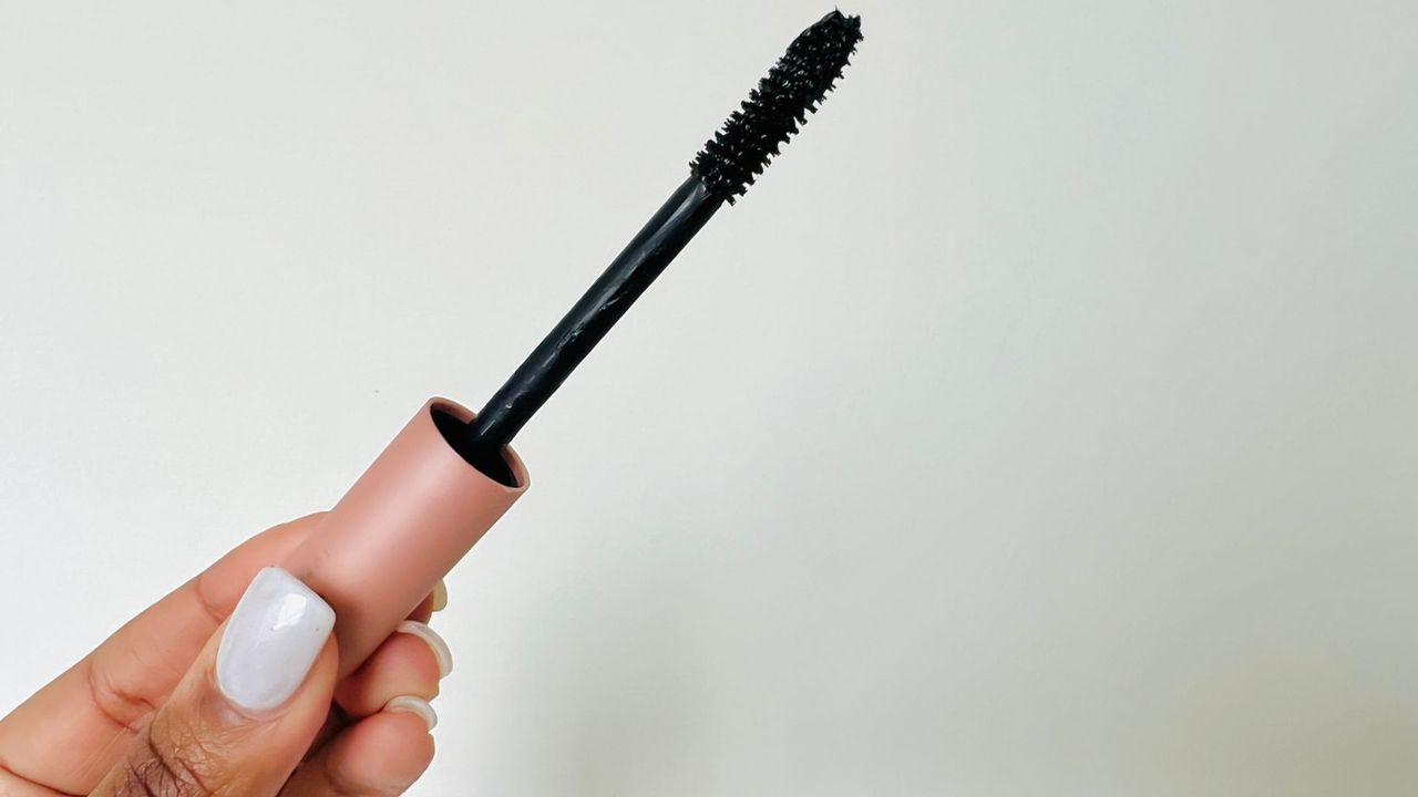 A person holding the L'Oreal Air Volume Mega Mascara wand and showing its brush, for the best L'Oreal mascara.