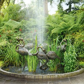 garden fountain with flamingo statues with surrounding trees