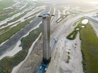 A massively tall super heavy booster towers over the flat Texas landscape as it is transported to the launchpad.