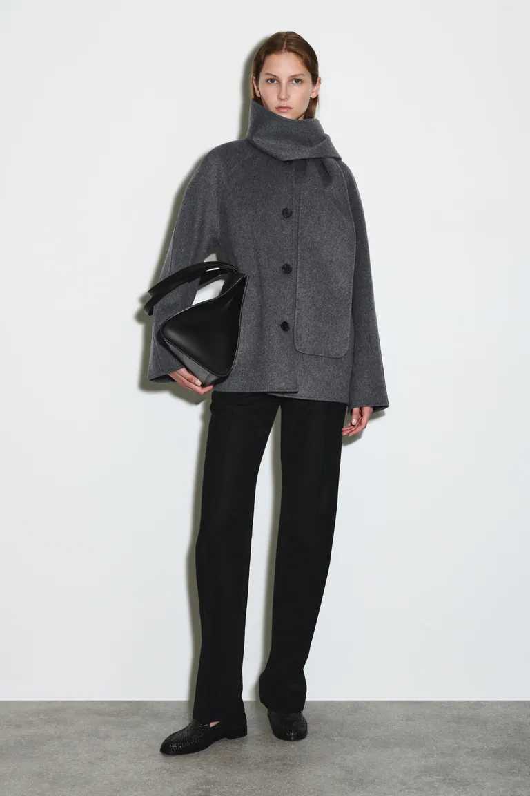 Woman wears grey scarf coat, black jeans and black loafers