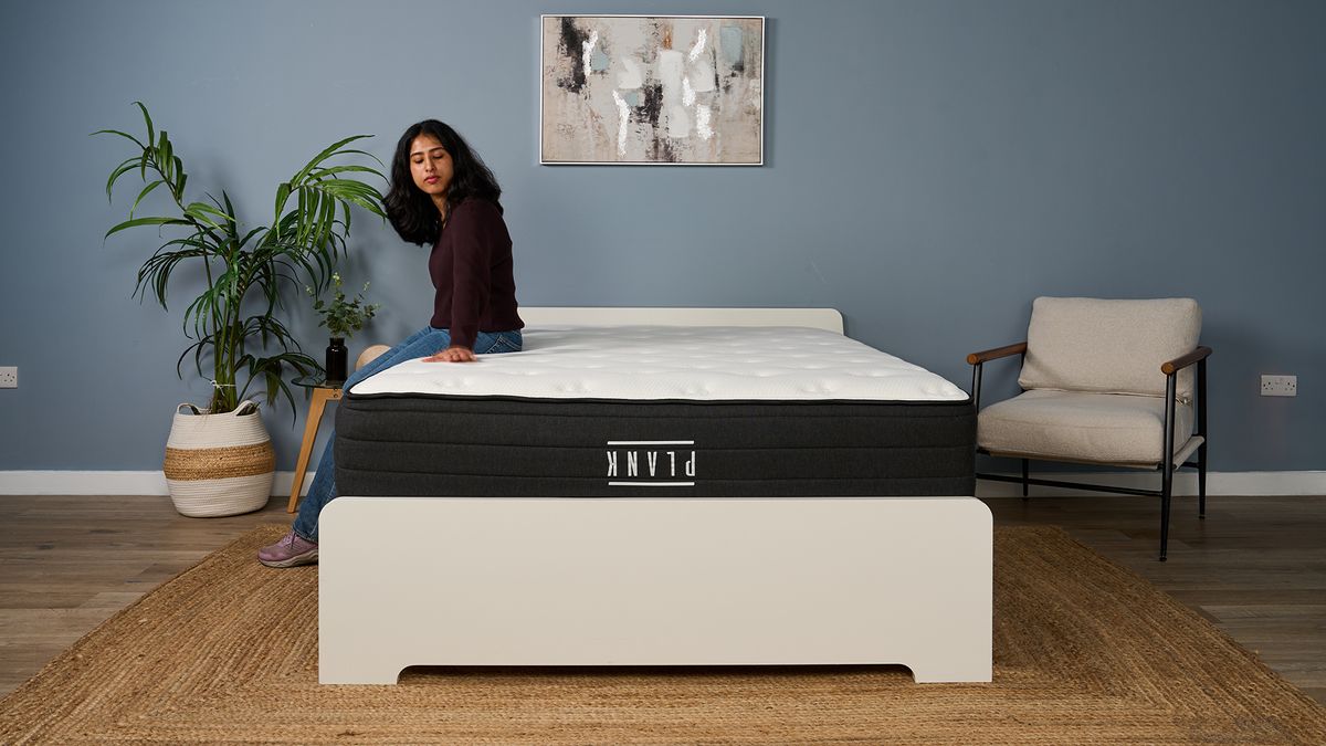 Mattress tester Becky George sits on the edge of the Plank Firm Luxe mattress (Firm side up), testing the support and comfort