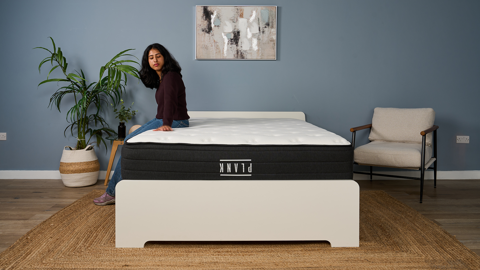 Mattress tester Becky George sits on the edge of the Plank Firm Luxe mattress (Firm side up), testing the support and comfort