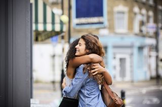 Two women hugging on the street outside, as the rules on whether two people can hug now have changed