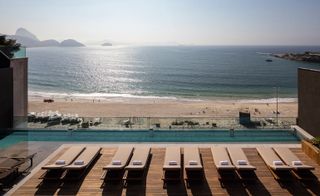 View of the beach from the rooftop at Emiliano Rio de Janeiro, Brazil. The rooftop features wooden decking, brown and beige lounge chairs and a swimming pool