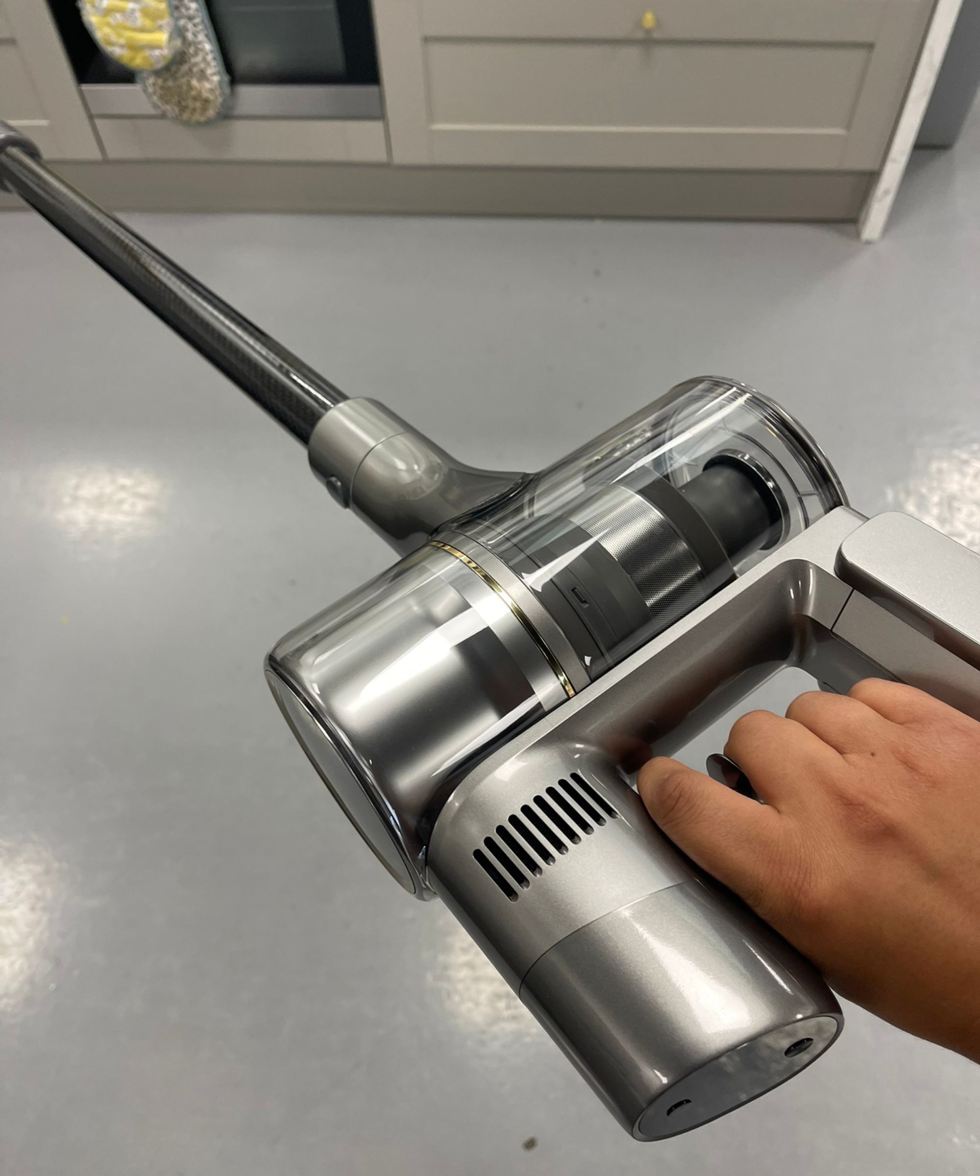 Hand holding the Dreame R20 cordless vacuum at an upwards angle above gray floor in Future test center.