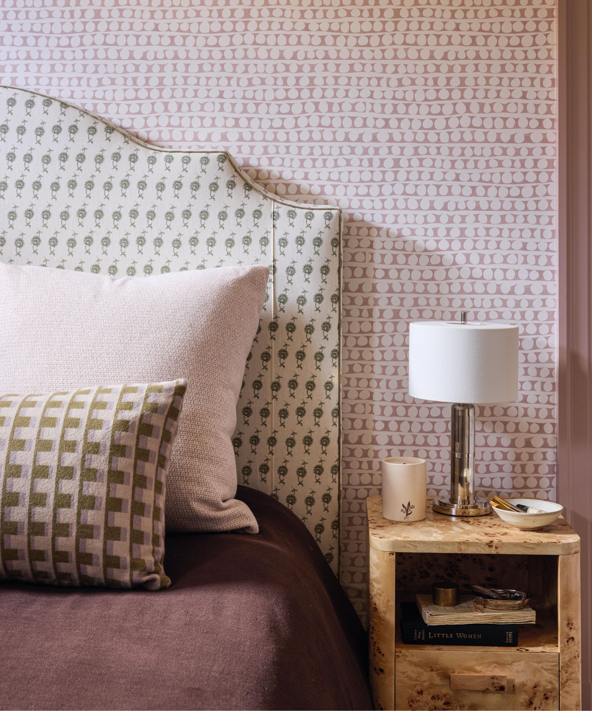 a plaid mauve and green bedroom with patterned walls, headboard, pillows and a small burl wood nightstand