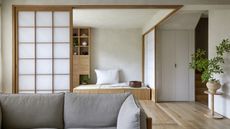 A neutral living room embracing Japanese "Muji" style with wooden floorboards, a gray sofa, and a screen door with frosted glass