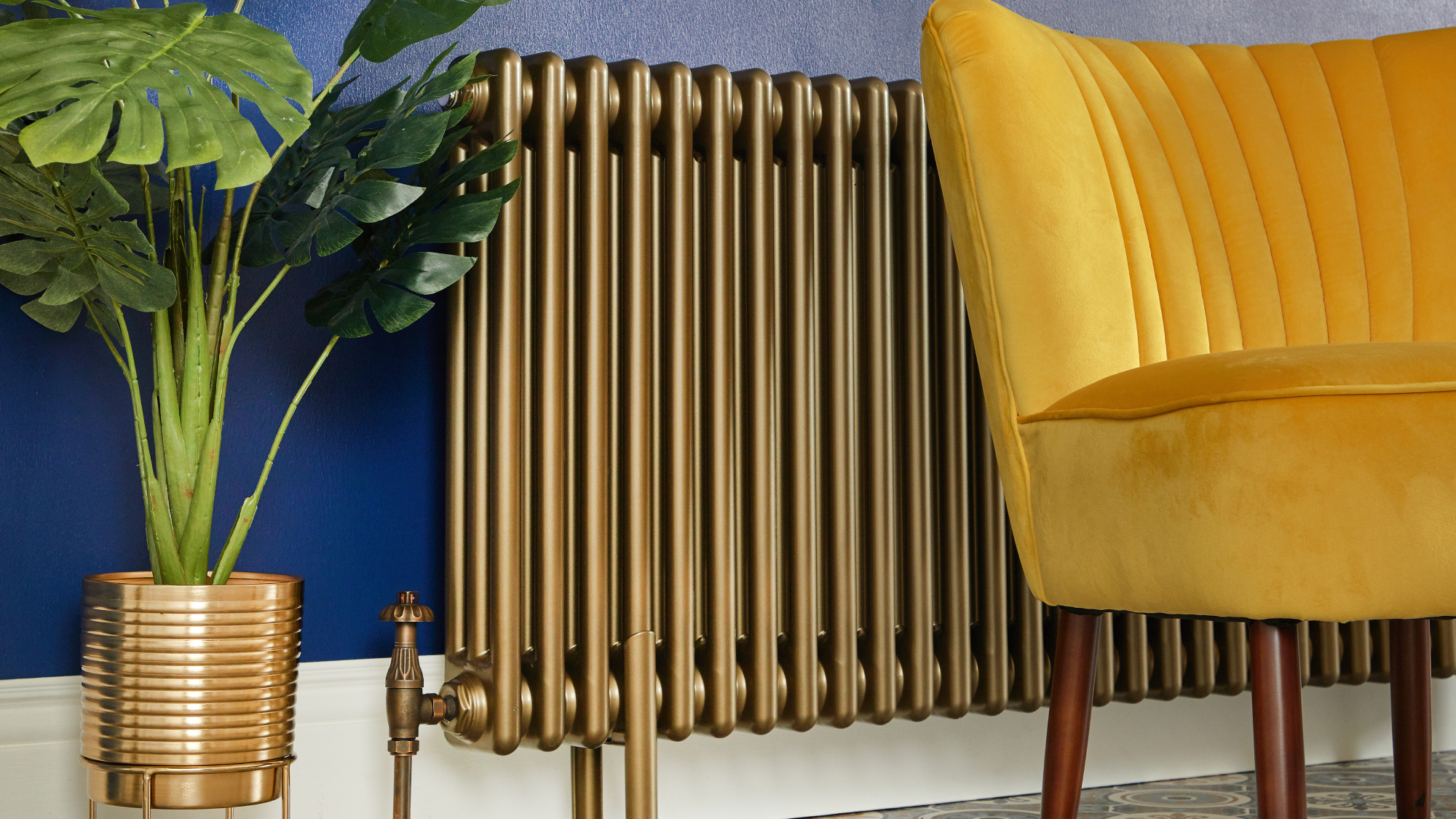gold radiator against blue painted wall with gold fabric armchair in front and potted plant in gold pot to side