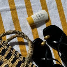 Beach towel with Beauty Pie SPF, straw bag and sandals