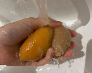 A hand rinsing two orange makeup sponges under a tap