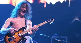 A shirtless Eddie Van Halen plays his sunburst signature Peavey Wolfgang onstage in 2005.