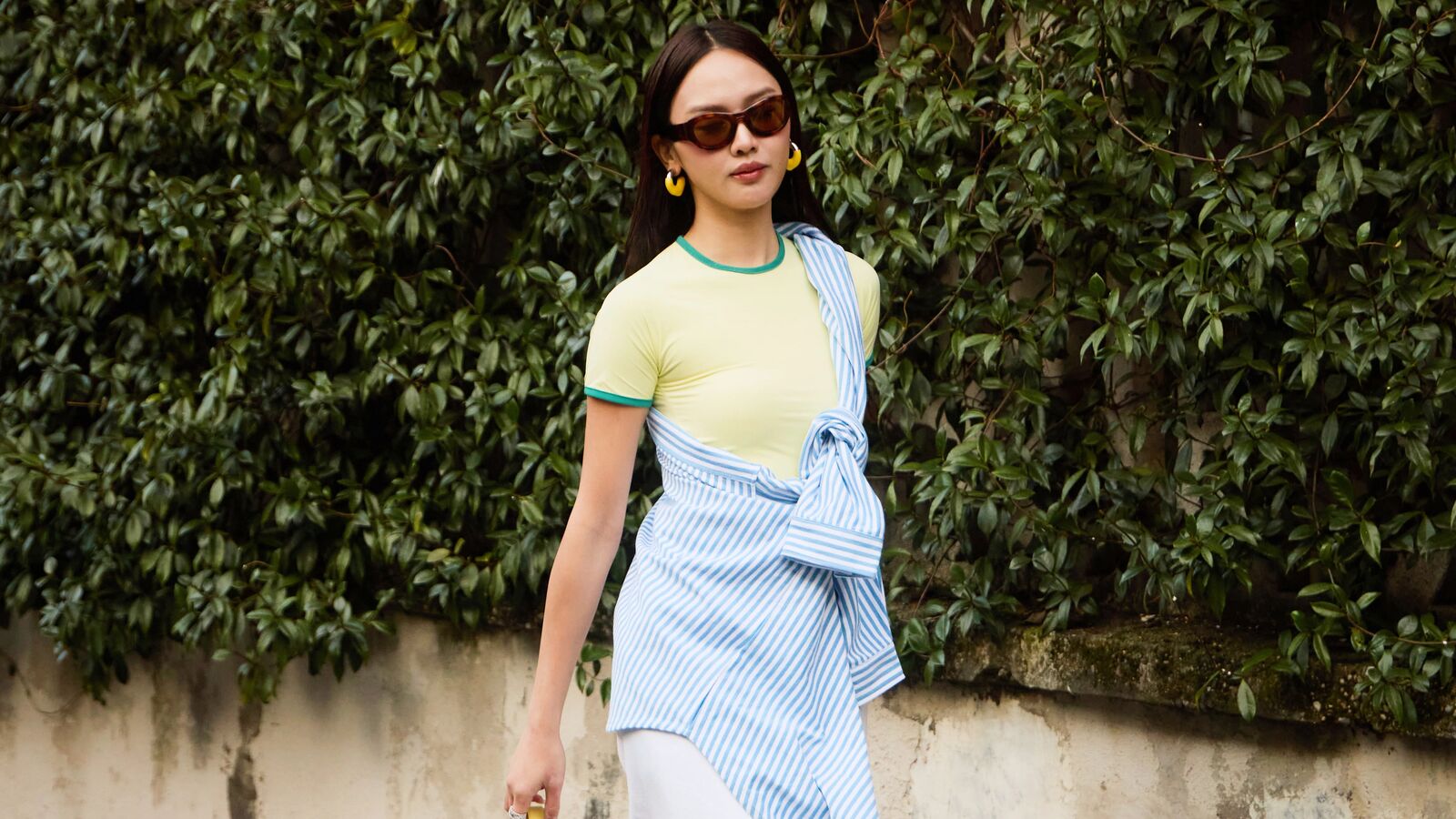 Woman wears yellow t-shirt, white skirt, green heels, and a button-down shirt tied around the chest. 
