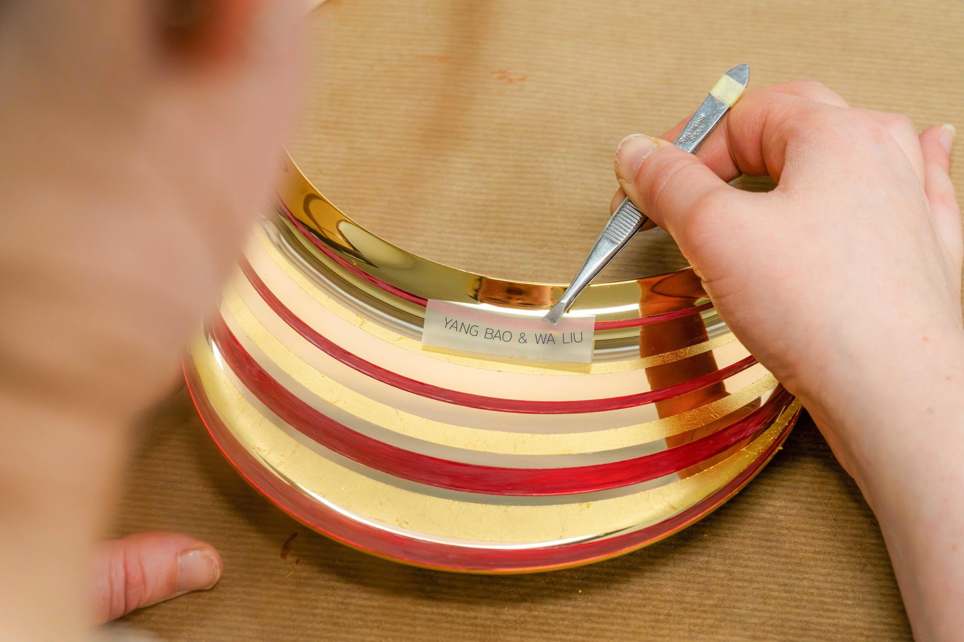 Person with tweezers adjusts name sticker on gilded speaker part