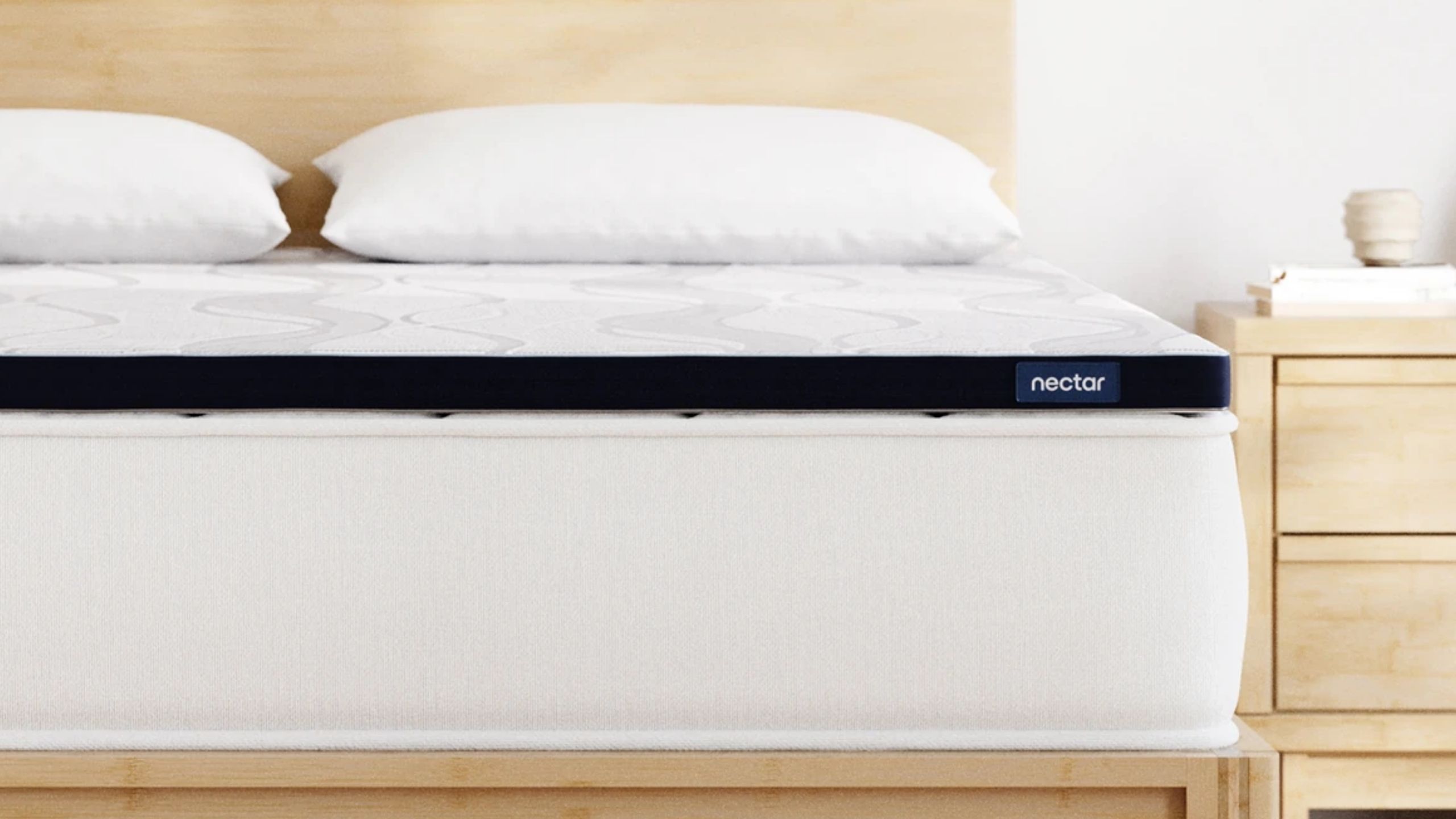Nectar Firmer Mattress Topper on a light wood bedframe beside a matching nightstand