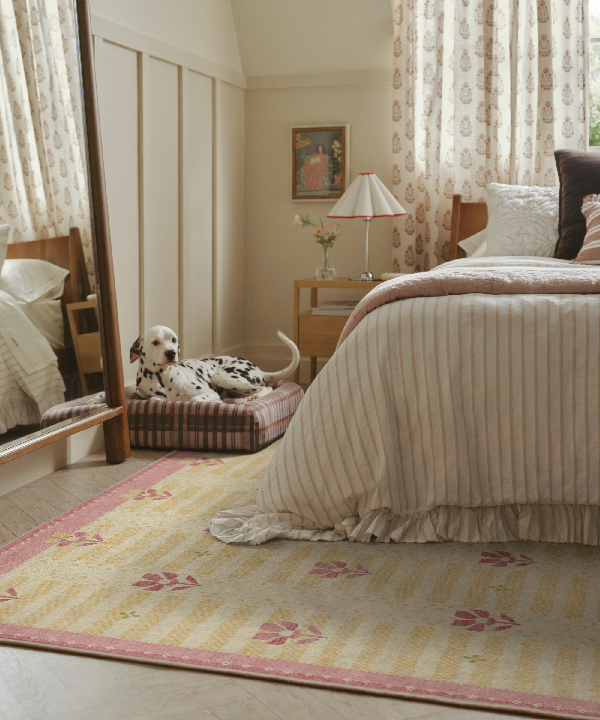 a bedroom with a floral rug, striped bedding on a bed, and a dalmatian sitting on a dog bed