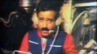 blurry photo of a man with a mustache wearing a blue vest and headphones