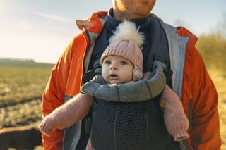 parent carrying a baby in a carrier out in the countryside