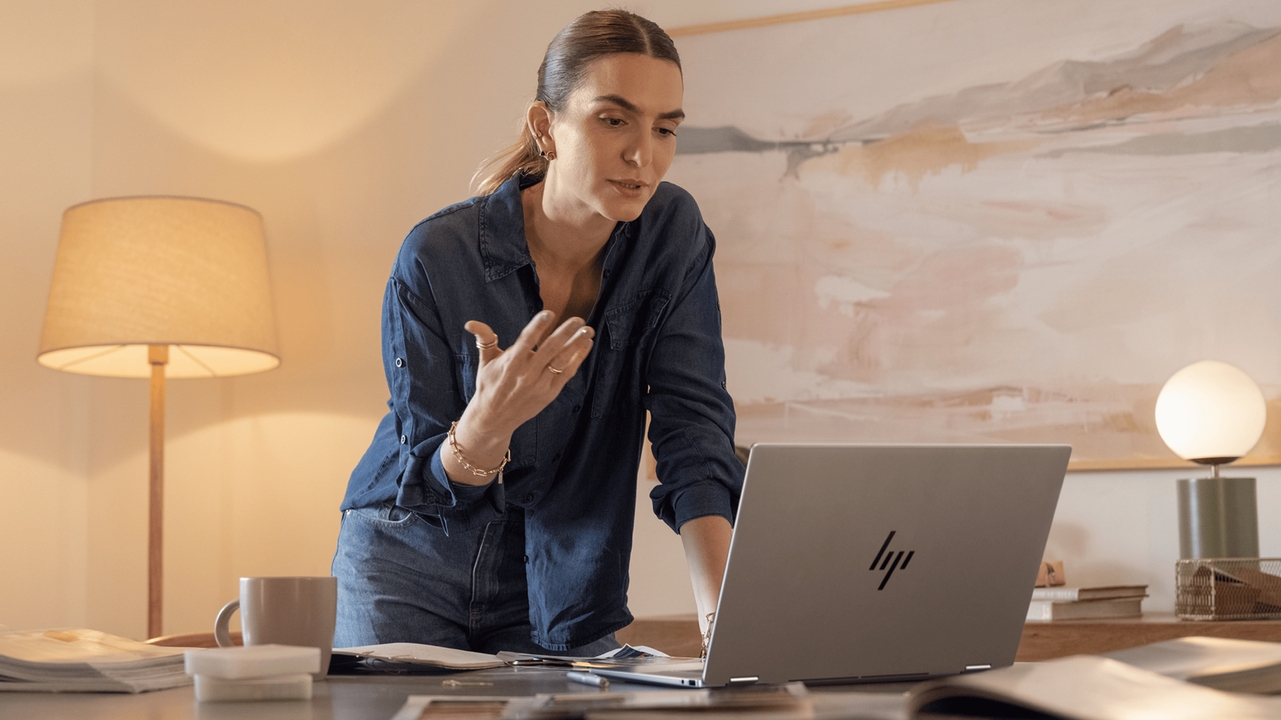 A woman stands at a desk looking at the HP OmniBook X Flip.