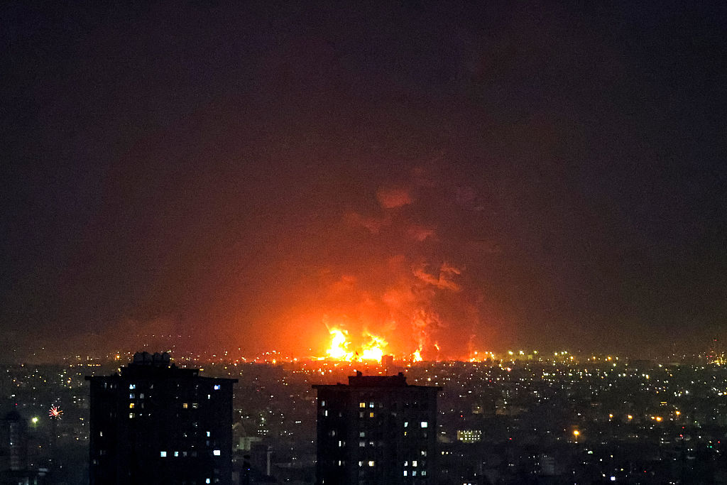 A glowing explosion is seen in the middle of a cityscape during the evening.