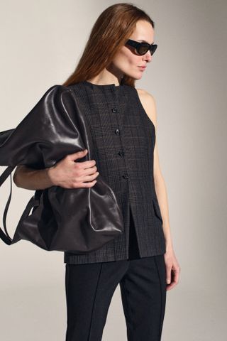 A Kallmeyer model wears a structured vest, black pants, and an oversize leather tote bag