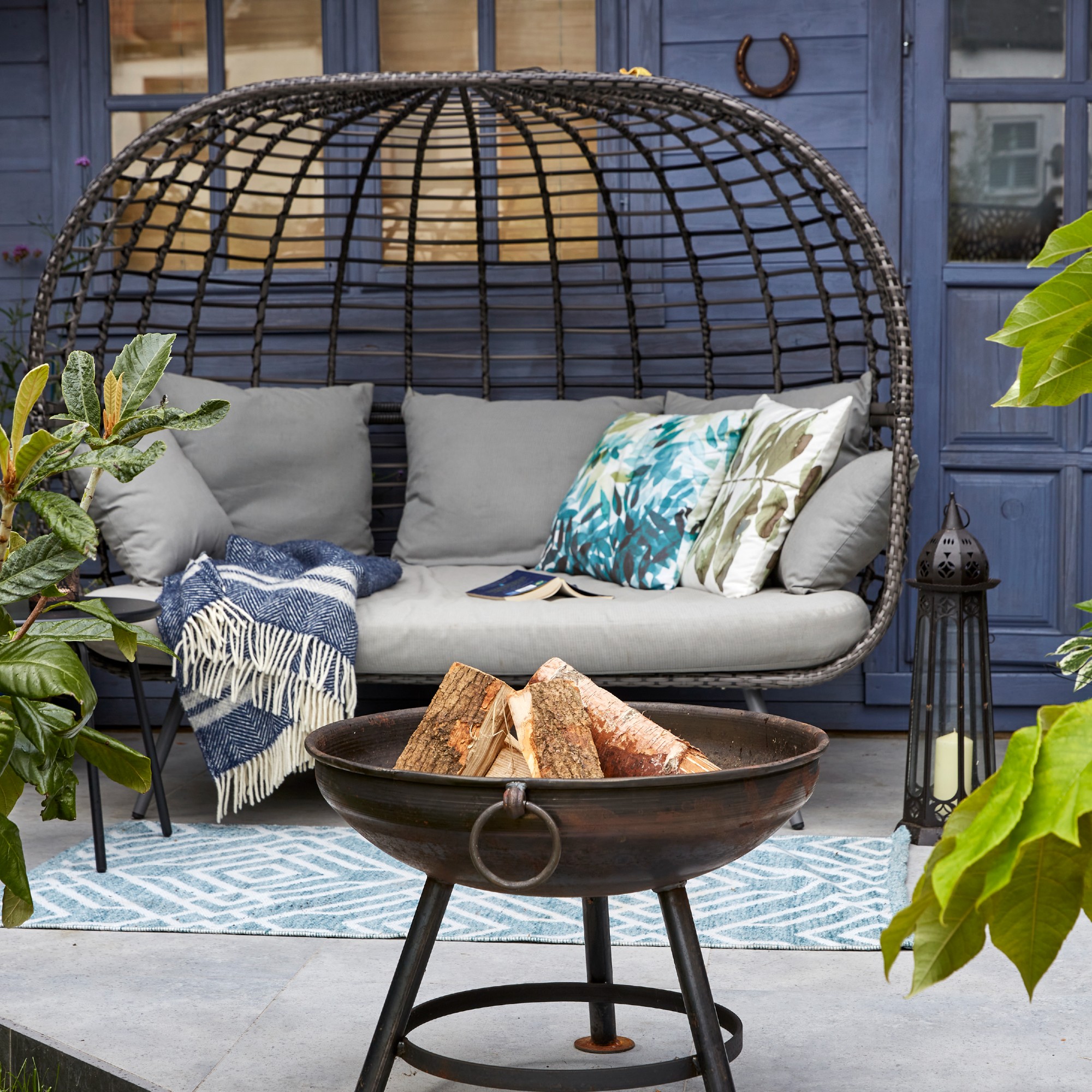 A patio with a black curved rattan outdoor sofa and a fire pit