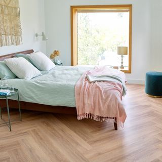 bedroom flooring ideas, pale aqua bedroom with pink and aqua bedding, laminate parquet flooring, large window, metal bedsides, macramé on wall, wall light
