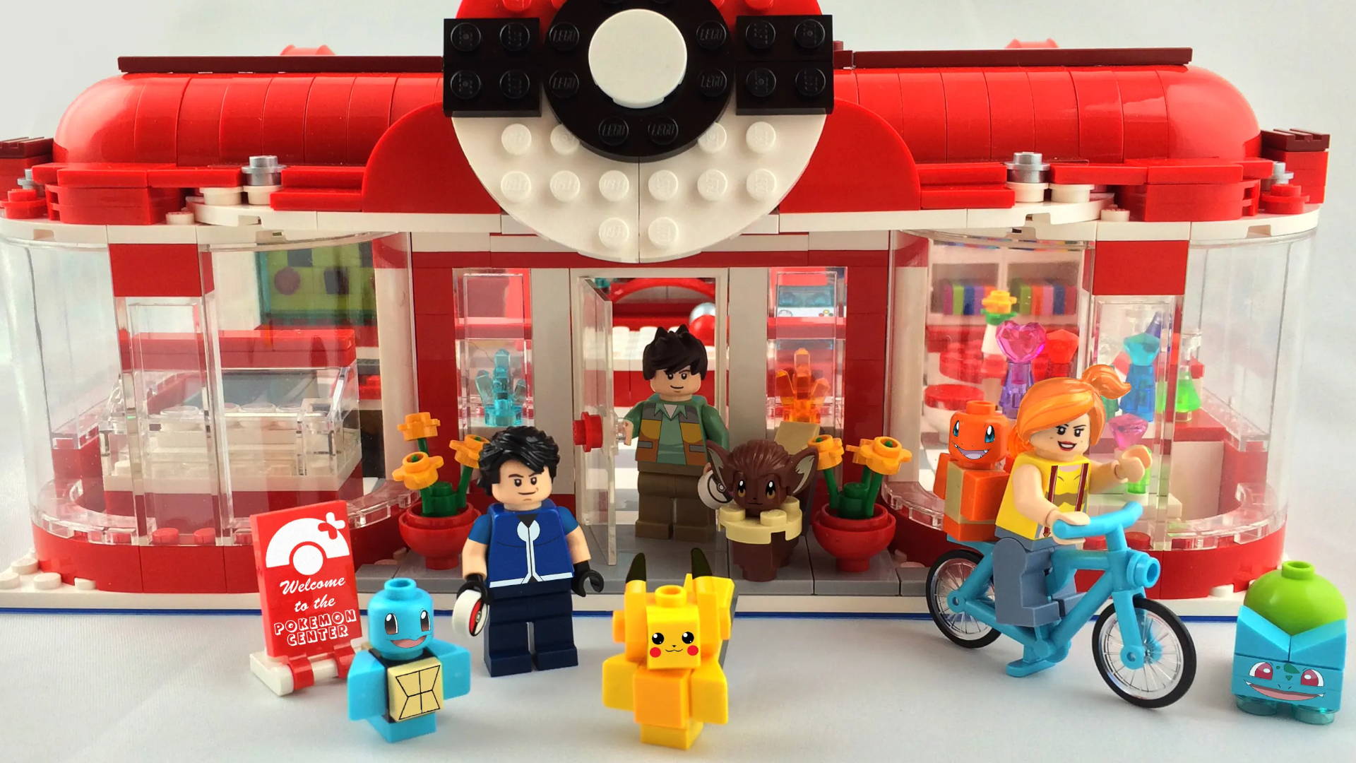 A selection of Pokemon and character minifigures outside a large, red-roofed Lego building against a white background