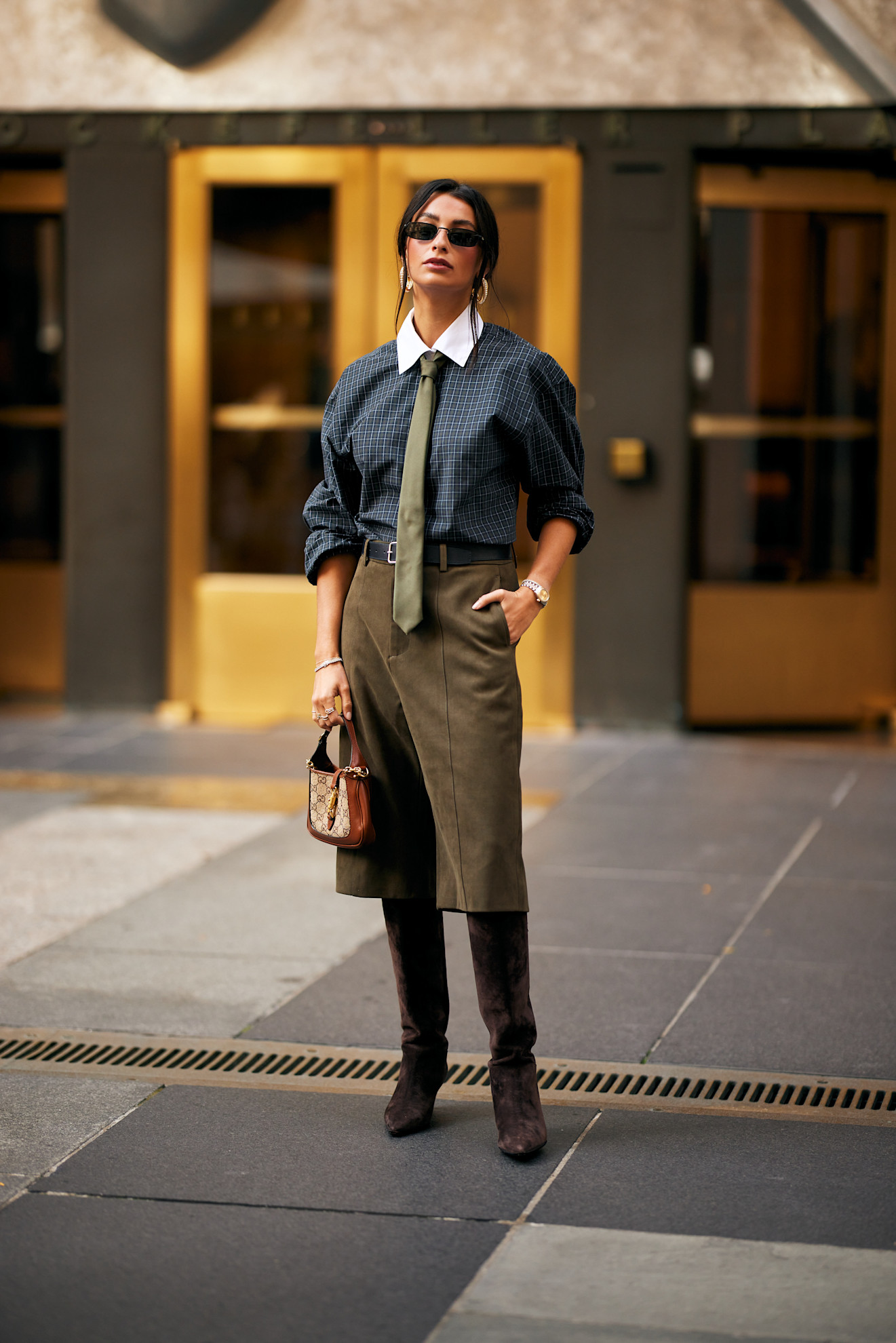 fashion week attendee wearing sunglasses, checked shirt, green tie, long shorts, and suede boots