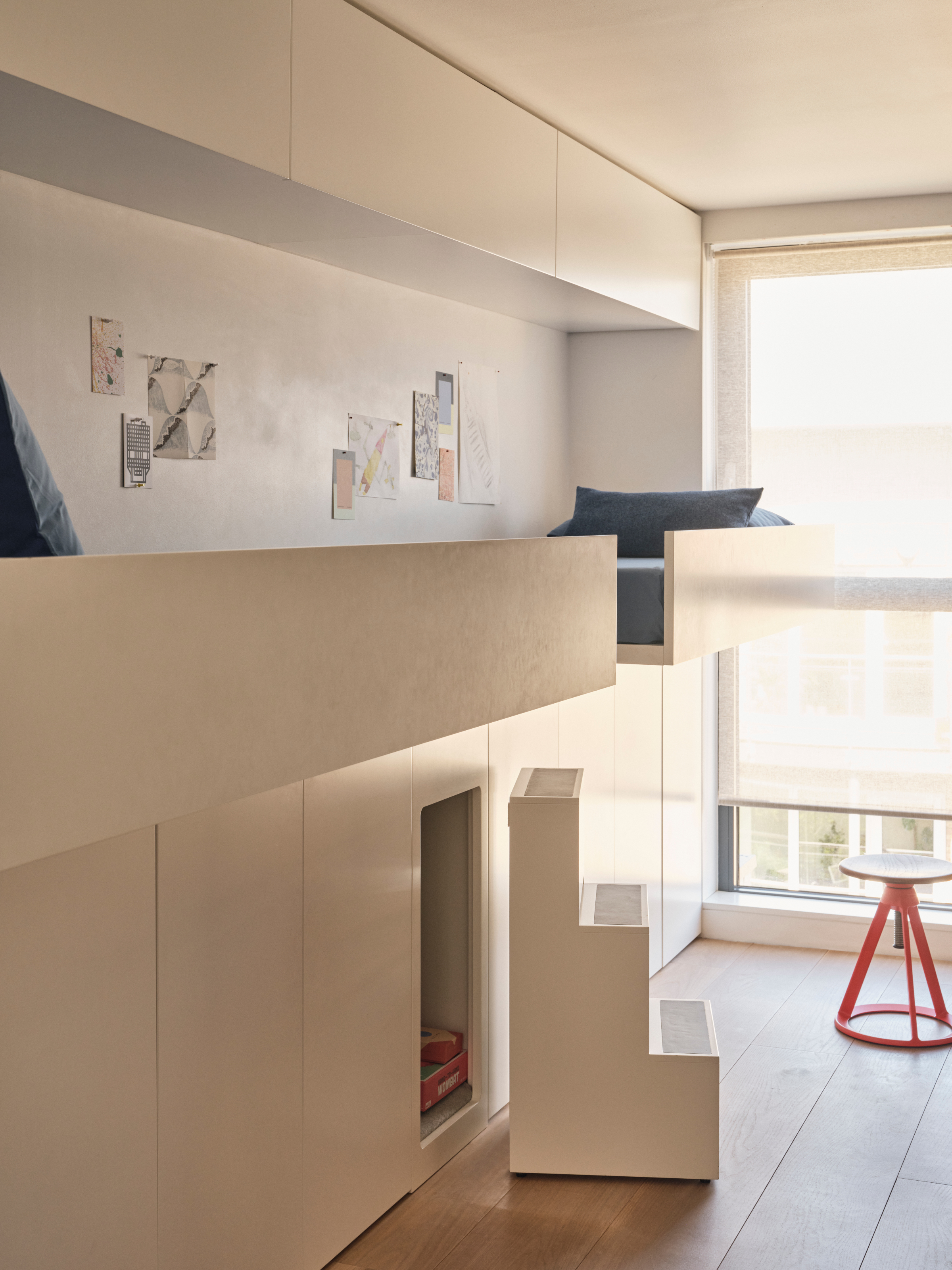 A children's bedroom with built-in joinery housing a cushioned seating area and hiding a nook disguised with a set of steps