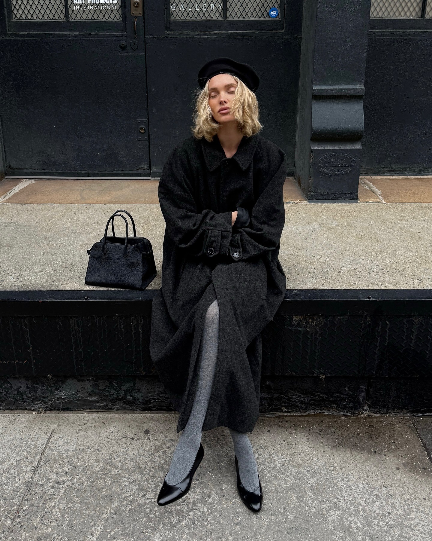 Elsa Hosk wearing a black coat, gray tights, and black flats