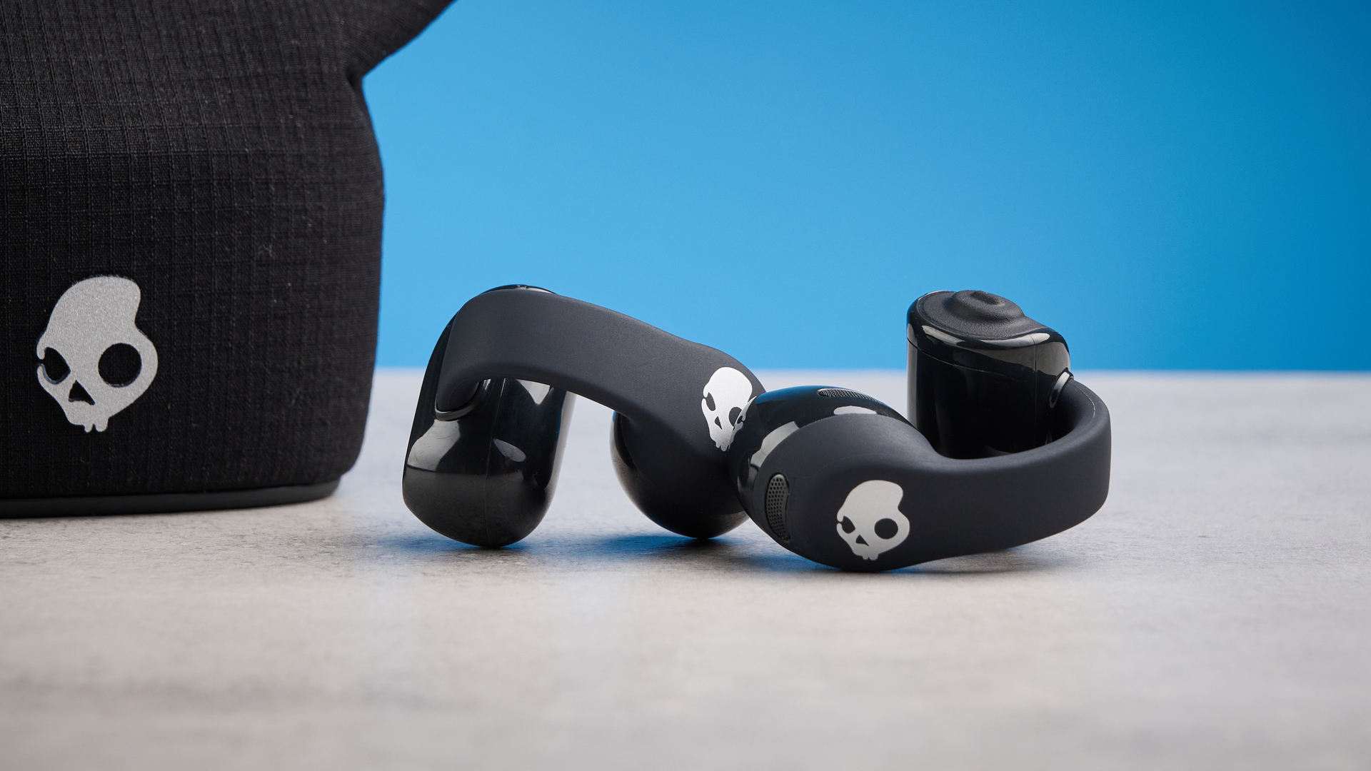 Skullcandy Push 720 Open in black and silver colorway with charging case photographed on a blue background