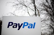 A close up photo of a white sign with the words PayPal displayed, with an overcast sky and bare tree branches in the background