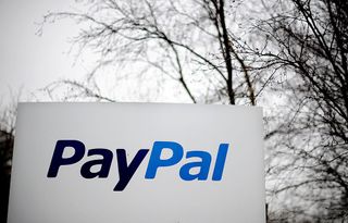 A close up photo of a white sign with the words PayPal displayed, with an overcast sky and bare tree branches in the background