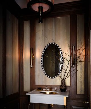 powder room with dark brown wood and metallic wallcovering, oval mirror and marble basin