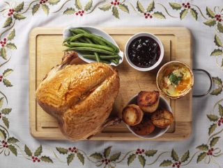 Turkey crown with beans, roast potatoes and cranberry sauce on a wooden board on a tablecloth with holly.
