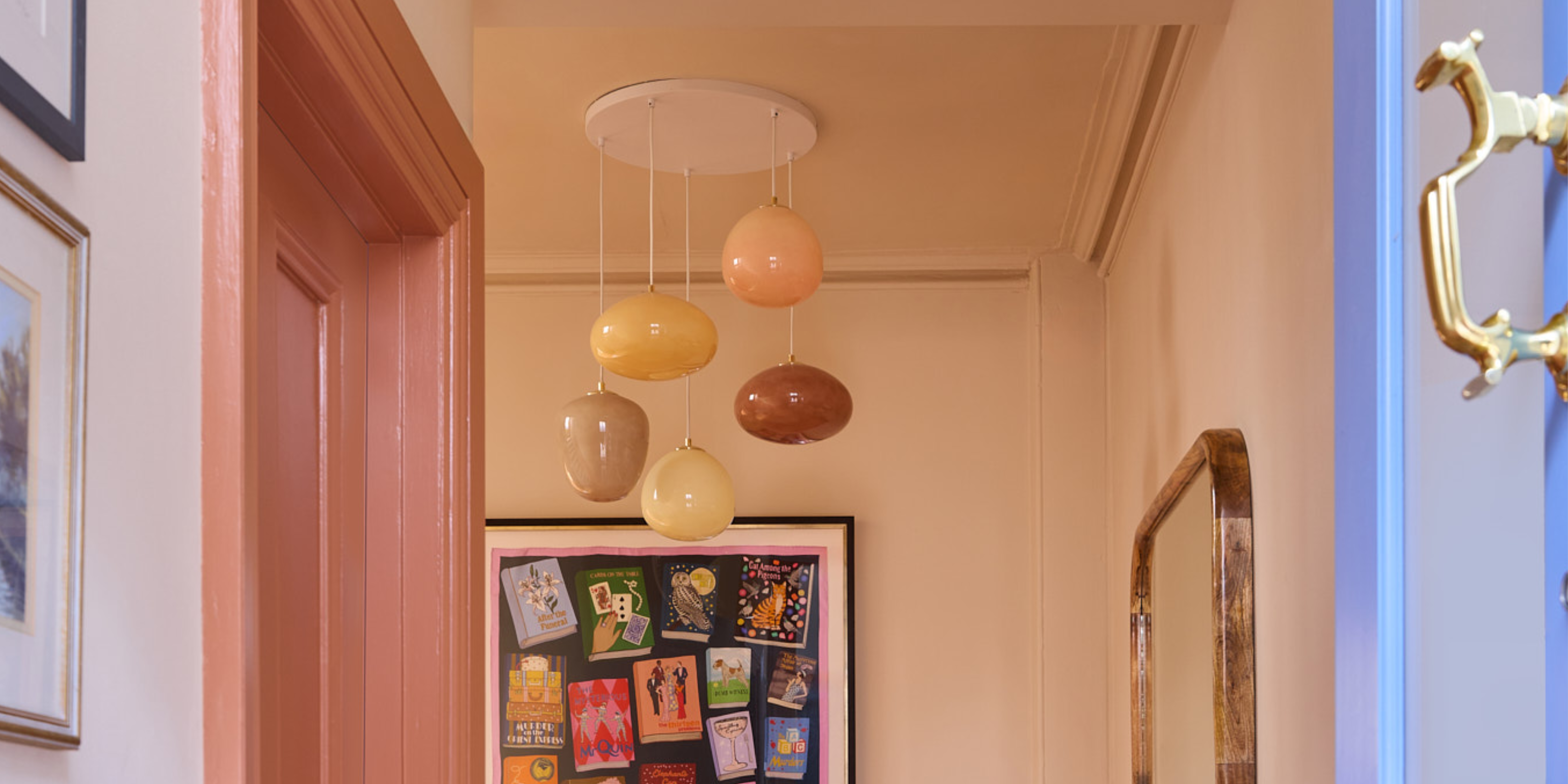 A view from an open front door into an entryway with pale pink walls and a multi-colored pastel pendant lighting fixture 