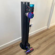Dyson V10 Konical Cordless Vacuum and Auto-Empty Dok sitting on wood-effect flooring in front of a white wall