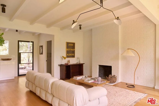 A modern living room with white brick walls, a plump white sofa, a small fireplace, and an arched lamp