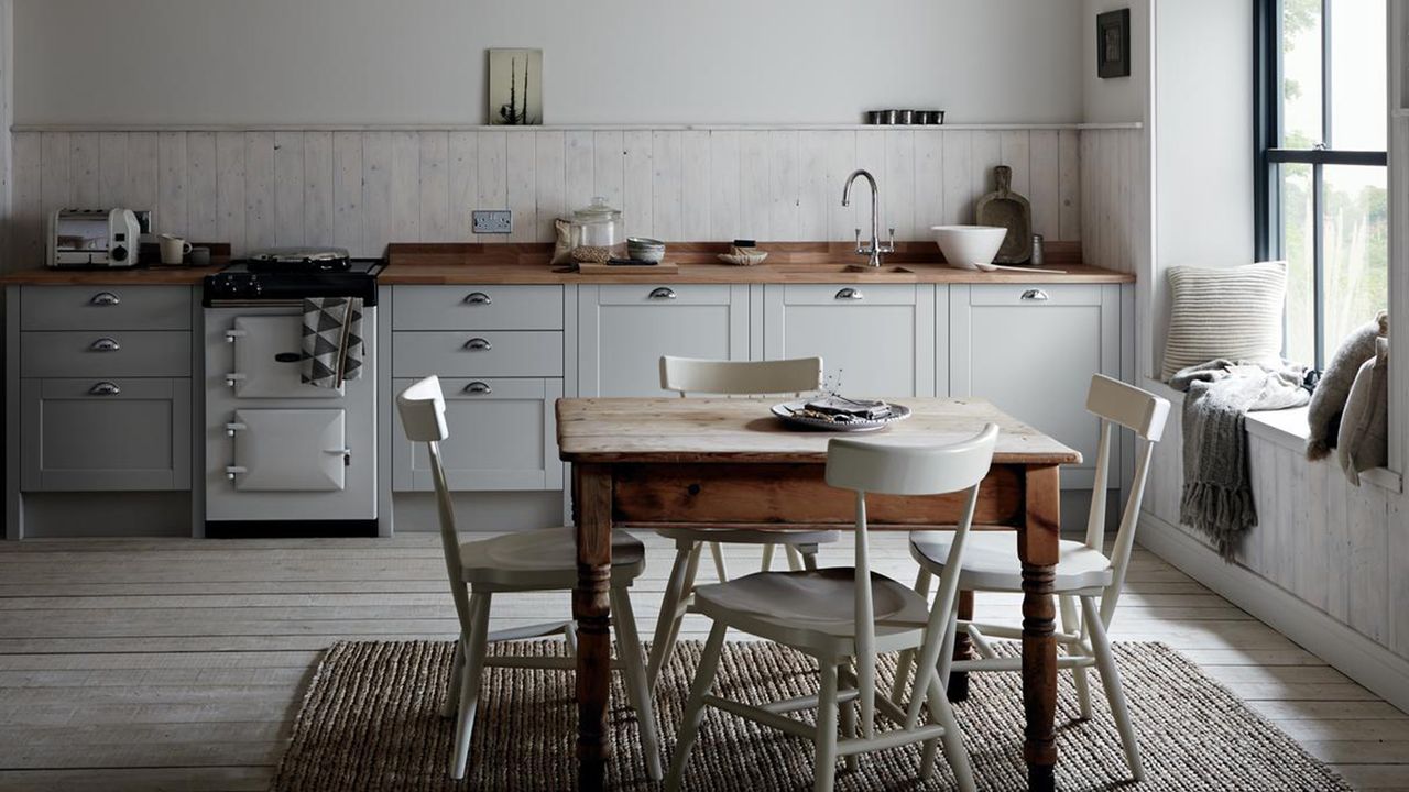 A rustic grey kitchen with dining table, range cooker and window seating with paneling on walls