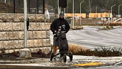 A man pushes his cart wearing shorts in the rain