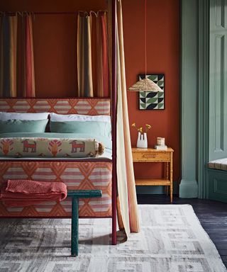 Four-poster bed with curtains, upholstered with orange fabric with pink geometric pattern and green bedding.