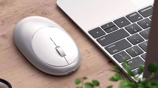 Satechi M1 Wireless Mouse on a wooden desk next to a MacBook