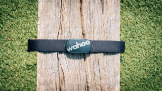 A black Wahoo Tickr heart rate monitor wrapped around a wooden bench, with the focus on the main part of the strap