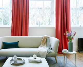 Red contrast drapes in lounge with neutral walls, sofa, and ottoman coffee table.