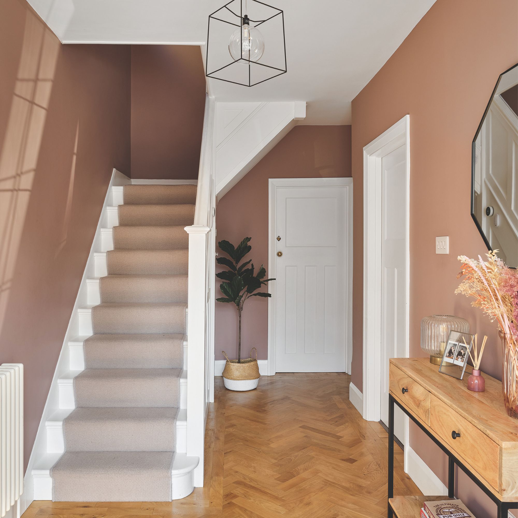 Pink painted hallway with white wooden stairs and a pink stair runner, and a console table on the left