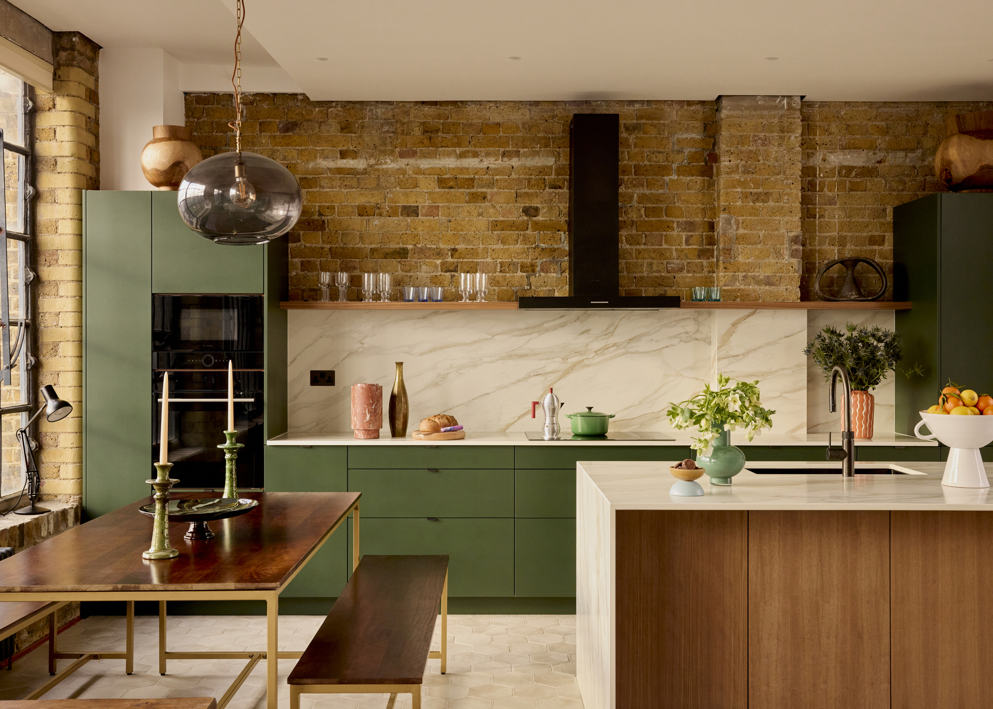A kitchen with bare brick walls, green slab cabinetry, and an island with a waterfall countertop