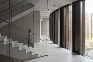 A staircase with silver metal railings, wire mesh walls and large windows in front of it.