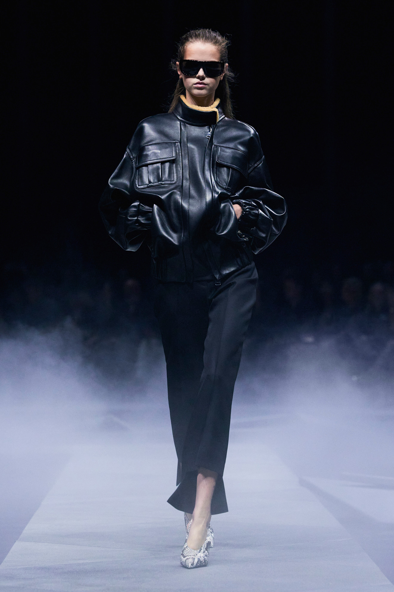 A woman at Khaite Spring 2026 wearing a black leather funnel neck bomber jacket and pants